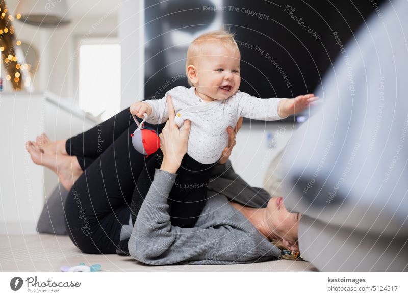 Happy family moments. Mother lying comfortably on children's mat playing with her baby boy watching and suppervising his first steps. Positive human emotions, feelings, joy.