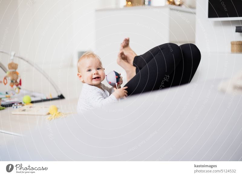 Happy family moments. Mother lying comfortably on children's mat playing with her baby boy watching and suppervising his first steps. Positive human emotions, feelings, joy.