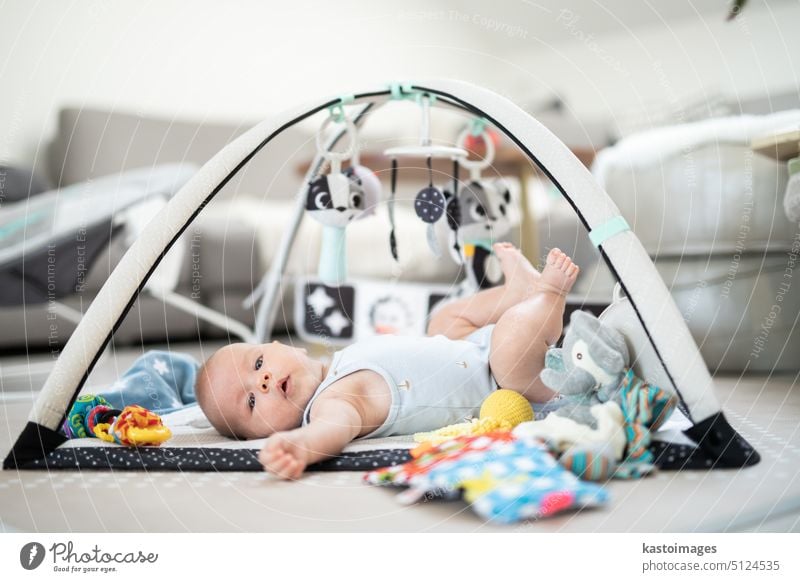 Cute baby boy playing with hanging toys arch on mat at home Baby activity and play center for early infant development. Baby playing at home newborn childhood