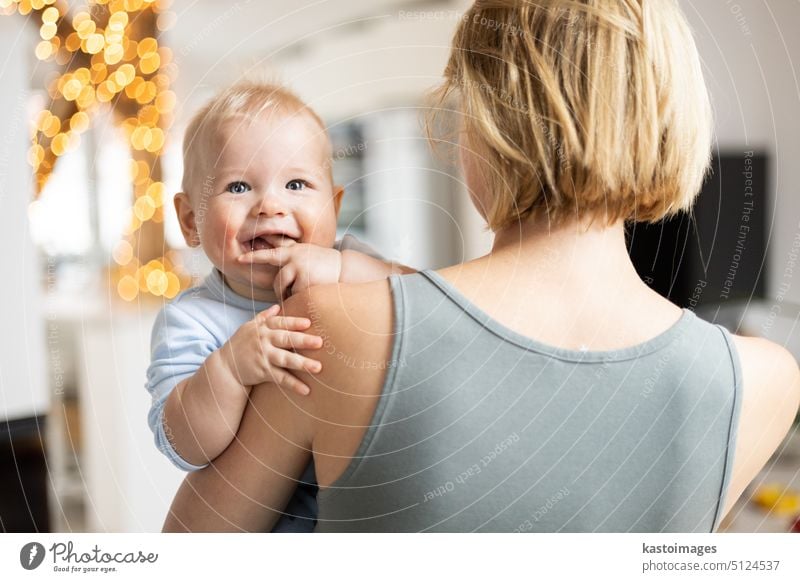 Blonde mother holding her adorable cheerful little infant baby boy. Cute infant child looking in camera and smiling at home family cute childhood togetherness