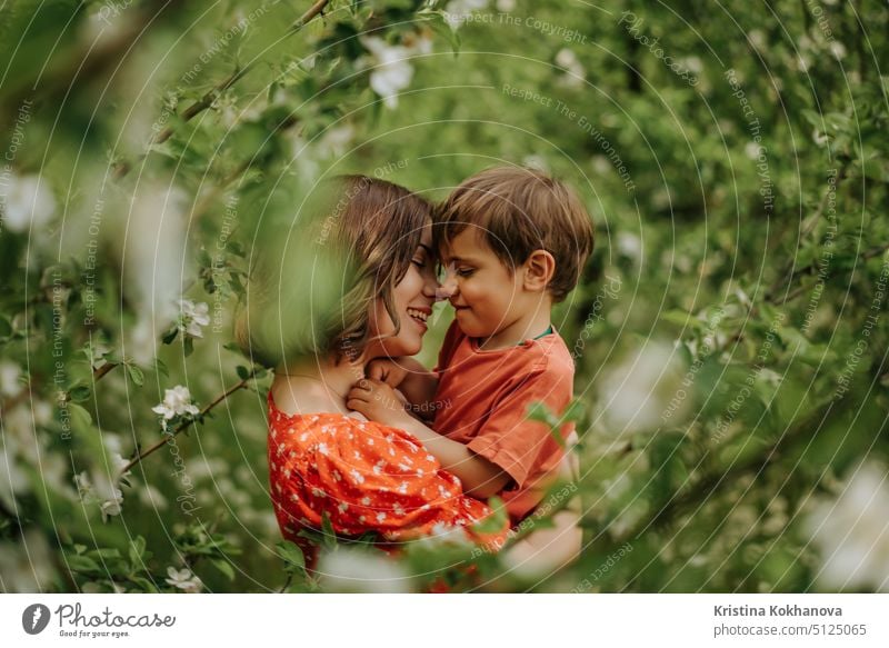 Portrait of happy mother and her baby boy. Beautiful touching scene of mom and son admires each other and sincerely smiles. Blooming garden in spring. Family, kiss, childhood concept.