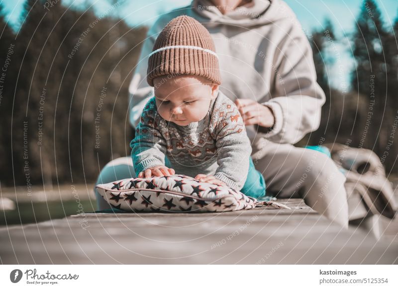 Happy family. Young mother playing with her baby boy infant oudoors on sunny autumn day. Portrait of mom and little son on wooden platform by lake. Positive human emotions, feelings, joy.