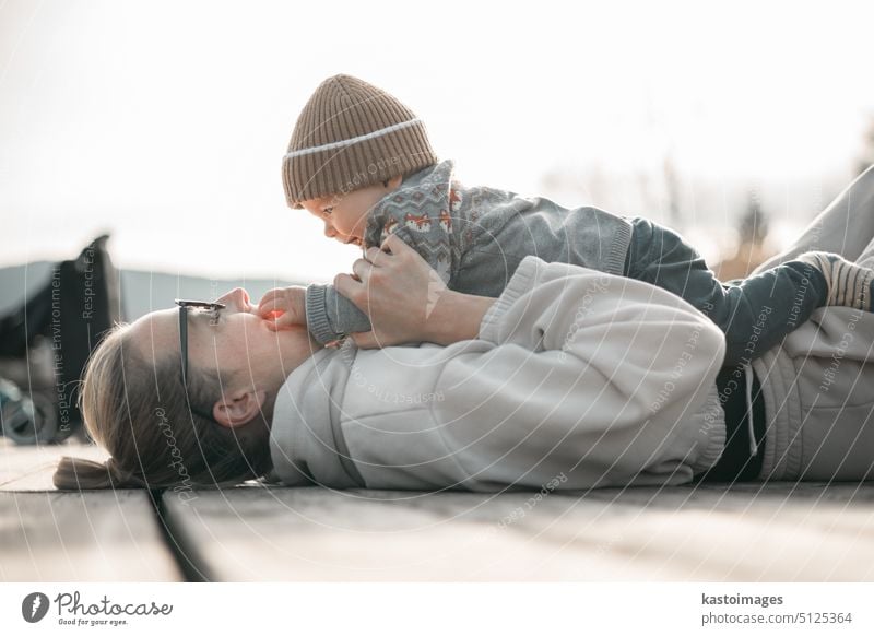 Happy family. Young mother playing with her baby boy infant oudoors on sunny autumn day. Portrait of mom and little son on wooden platform by lake. Positive human emotions, feelings, joy.