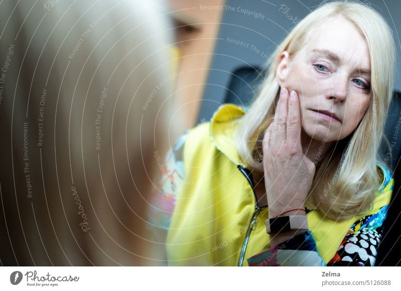 Portrait of middle-aged woman looking at her face in mirror, skin aging concept mature female sad beauty care checking wrinkles makeup blond hair closeup