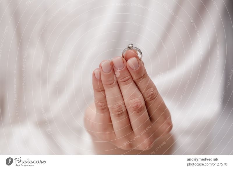 female hand holding wedding ring made of white gold and diamonds on a white background. Luxury expensive proposal ring. Bride in wedding day. accessory jewelry