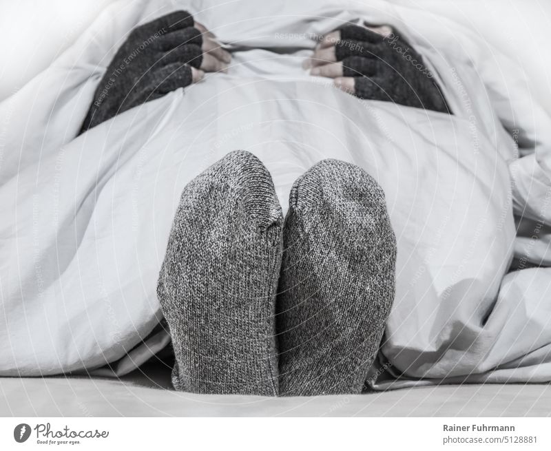 A person is lying in a bed. She has thick socks and gloves on. Bed Woman Cold chill Freeze Gloves Winter Frost Bedclothes Heating heating costs Expensive Energy