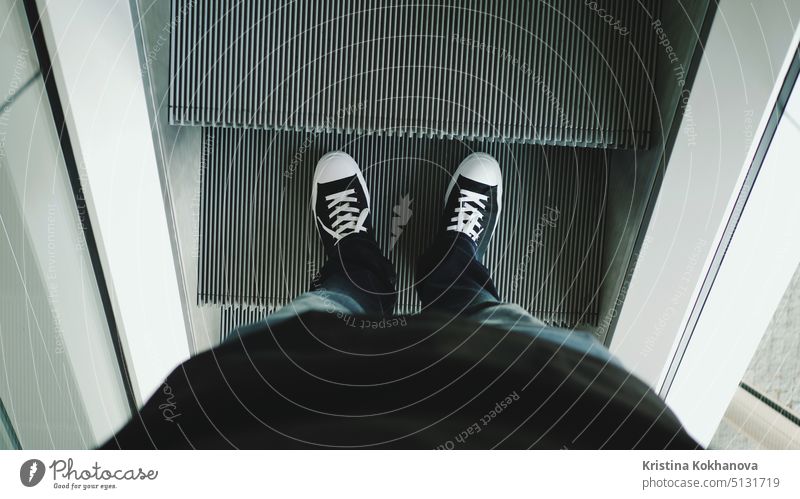 Closeup top view on man legs in sneakers traveler using moving escalator at airport terminal. people mall shoes commuter modern motion movement shopping