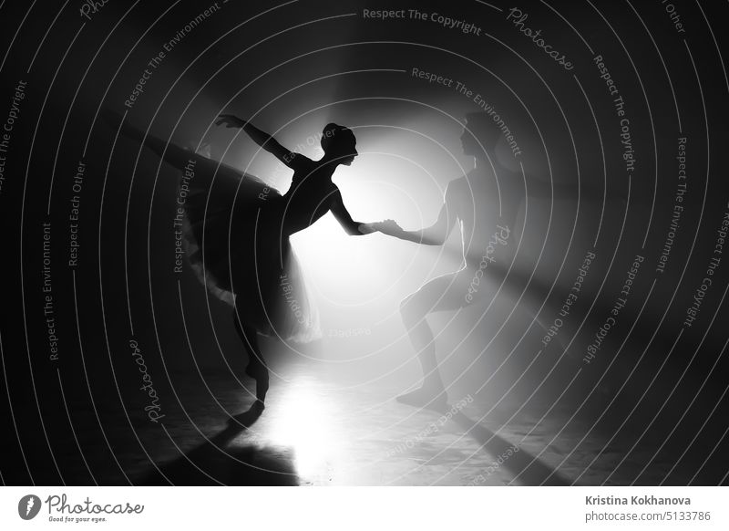 Professional ballet couple dancing in spotlights smoke on big stage. Beautiful young woman and man on floodlights background. Emotional duet performing choreographic art.