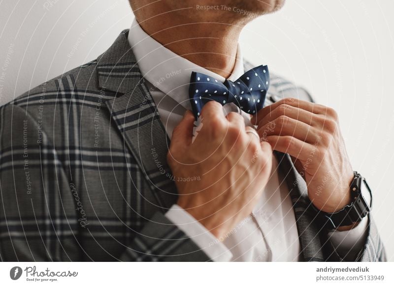 Man the groom in a wedding formal costume with butterfly. Suit, Hands, care, tie, to correct, to adjust, fashion, bow. Handsome business man in a suit. Portrait of sexy man