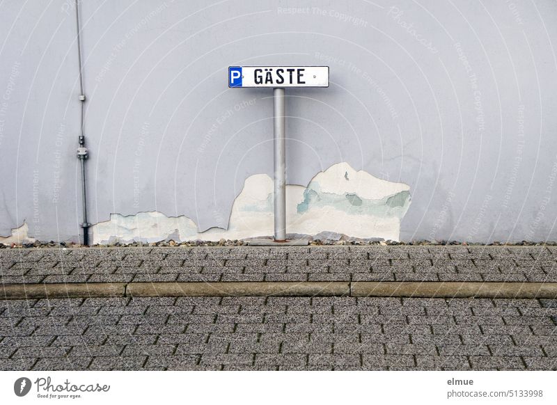 Sign with P guests standing in front of a gray wall with peeled plaster on concrete pavement / guest parking lot Parking lot house wall Guest parking Clearway