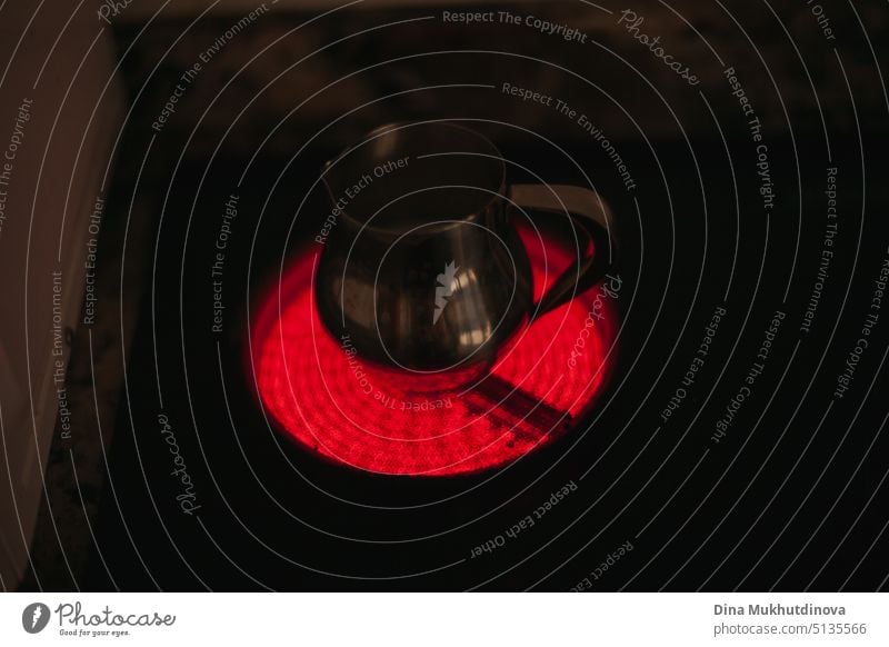 Red electric flame of kitchen stove with a metallic milk jug on it against black background. Gas crisis and electricity bills. electrical economy energy design