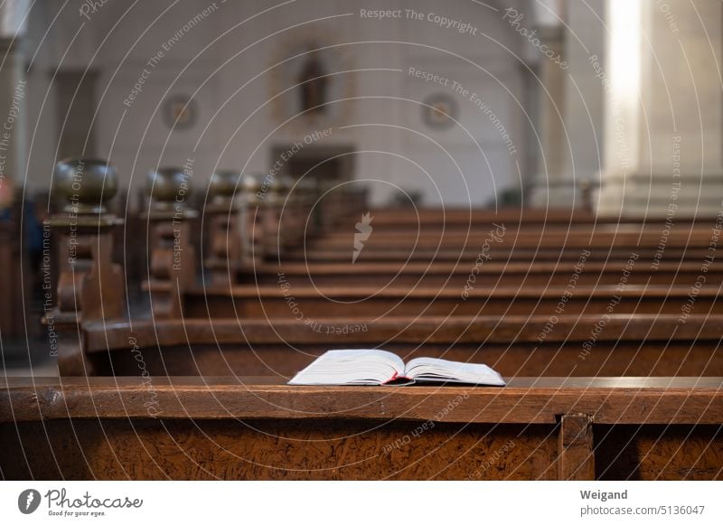 View over pews made of dark wood, while in the foreground or focus an opened bible or hymnal lies open on the wooden bench Bible Song book Church Sanctuary