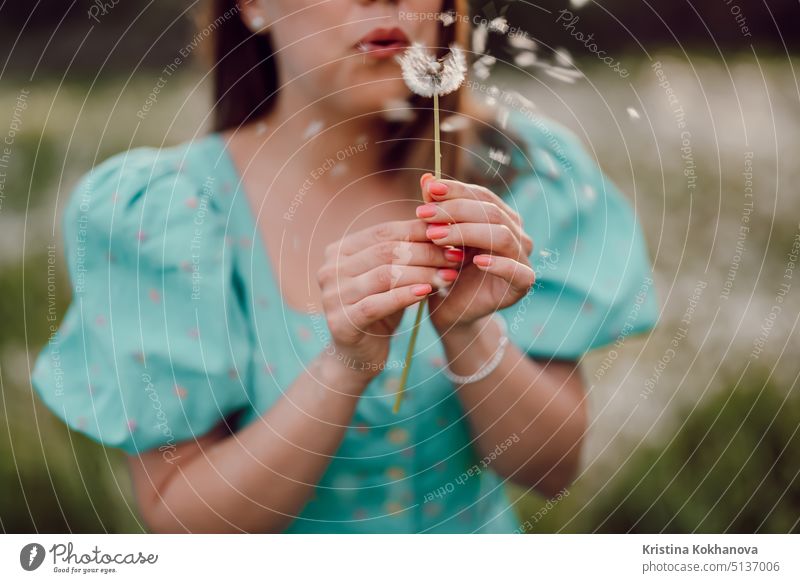 Happy woman beautiful blowing on dandelion in park. Girl in vintage blue dress. Wishing, joy concept. Springtime, aesthetic portrait adult attractive beauty