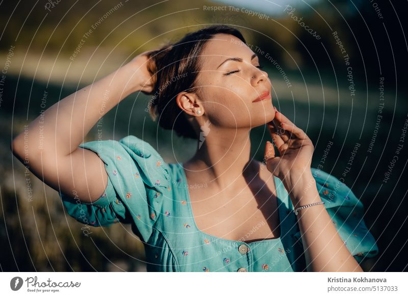 Portrait of young rural elegant woman posing on nature background. Sexy languid lady touching hair, enjoying summertime, sun rays. Vintage styled dress. vintage