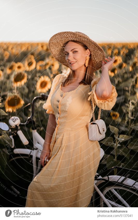 Attractive woman in timeless dress with retro styled bicycle in sunflowers field. Vintage fashion, amazing adventure, countryside activity, healthy lifestyle.