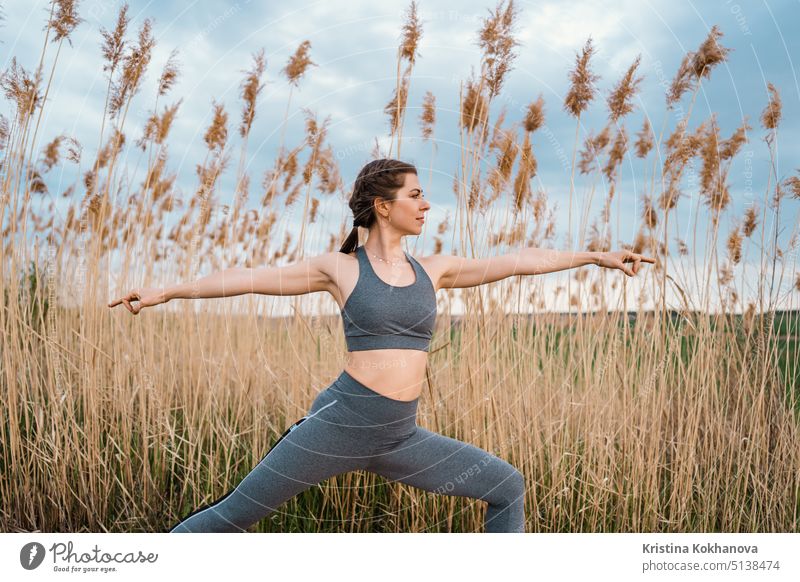 European woman doing yoga exercise on reed natural background. Concentrated girl training at summer outdoors. Pastel colors, unity with nature, balance, lifestyle concept.