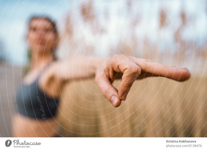 European woman doing yoga exercise on reed natural background. Concentrated girl training at summer outdoors. Pastel colors, unity with nature, balance, lifestyle concept.