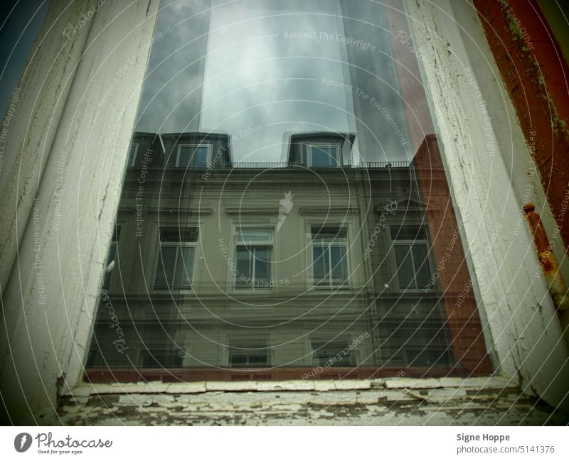 A window pane with a brittle wooden frame reflects the old town house opposite on a gloomy day. reflection Window Window frame Wood Old Building Facade