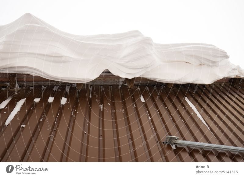 snow looking like soft ice cream or whipped cream hangs over roof of hall covered with brown sheet metal Soft ice cream snow on the roof snow layer thick snow