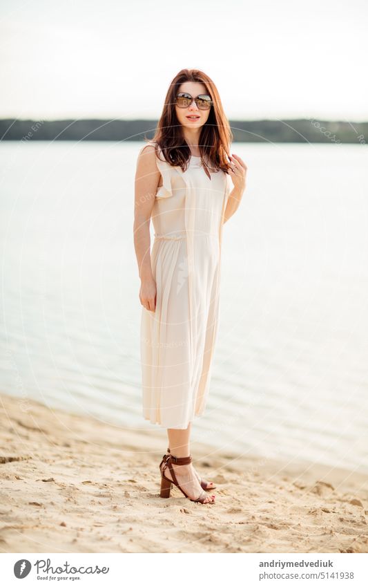 Pretty young woman with dark hair near at the beach near the lake in dress and sunglasses. concept of happy holiday and resort time pretty travel vacation water