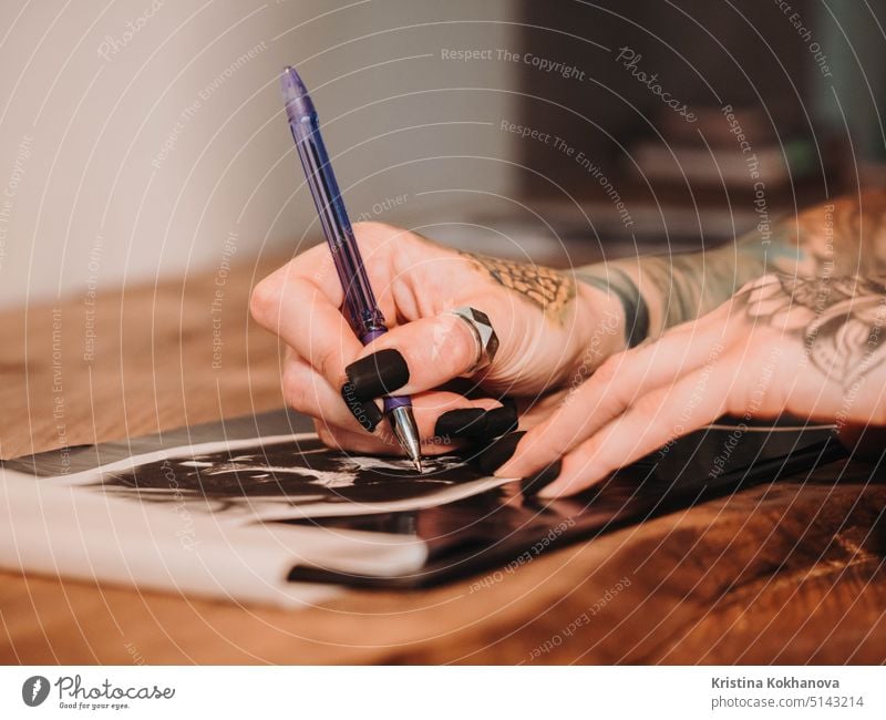 Tattoo artist drawing illustration of skull inside ink studio. Woman with black nails and rings at work. New fashion lifestyle artistic trends concept . Warm cinematic filter.