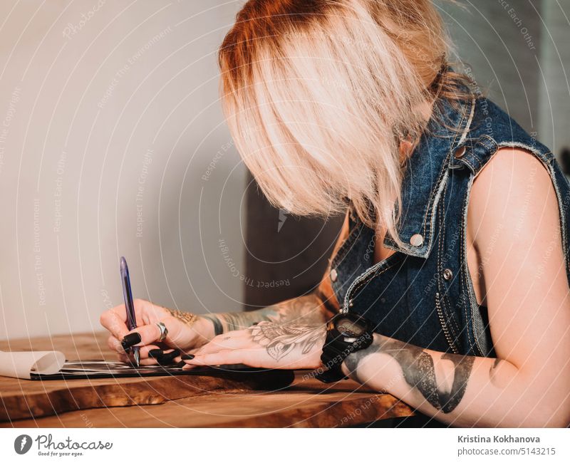 Tattoo artist drawing illustration of skull inside ink studio. Woman with black nails and rings at work. New fashion lifestyle artistic trends concept . Warm cinematic filter.