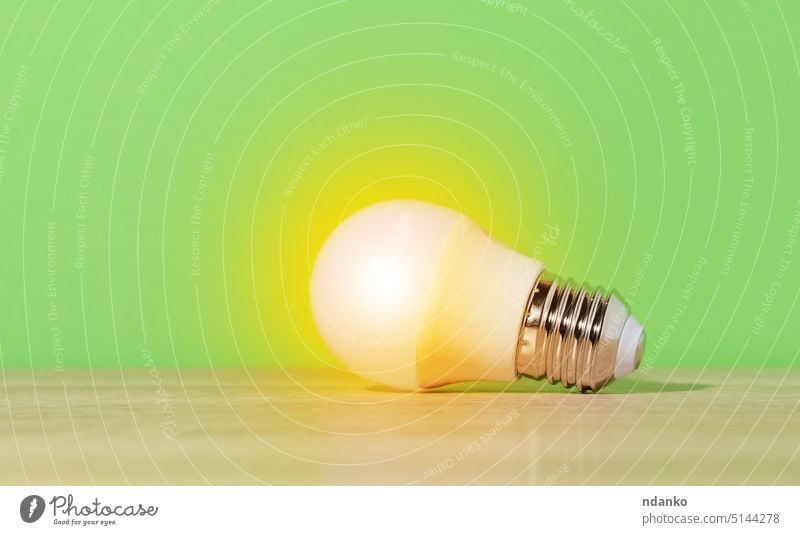 A glass white lamp shines with yellow light on a green background. New idea bulb energy innovation technology concept electricity invention power glasses