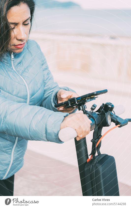 Beautiful latina woman riding her motorized scooter in the city, activating smart phone app. active casual close up day e-scooter eco electric electric mobility