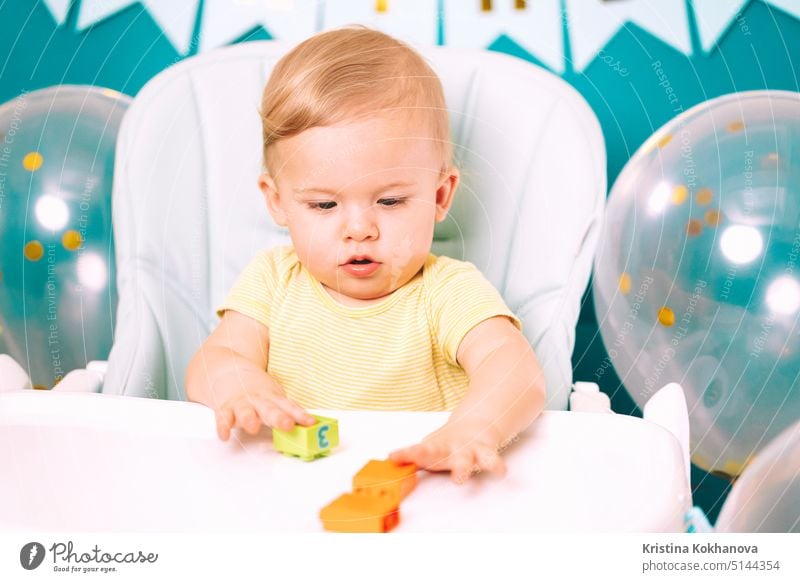 Cute baby boy sitting in his chair and playing with colorful bricks. Birthday handsome toddler child with big eyes portrait. Funny kid. caucasian happy home