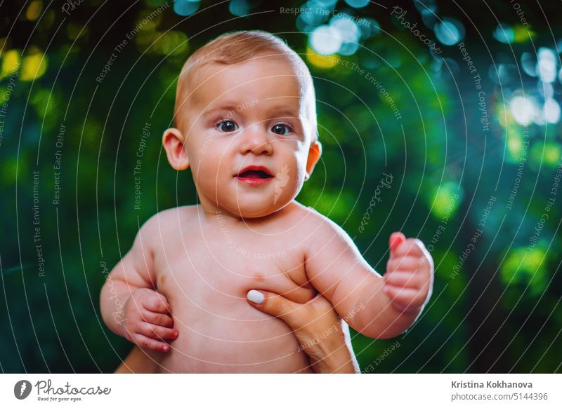 Handsome baby boy looking to camera and smiling on green forest background. child cute beautiful face childhood play eyes person cheerful playing funny kid