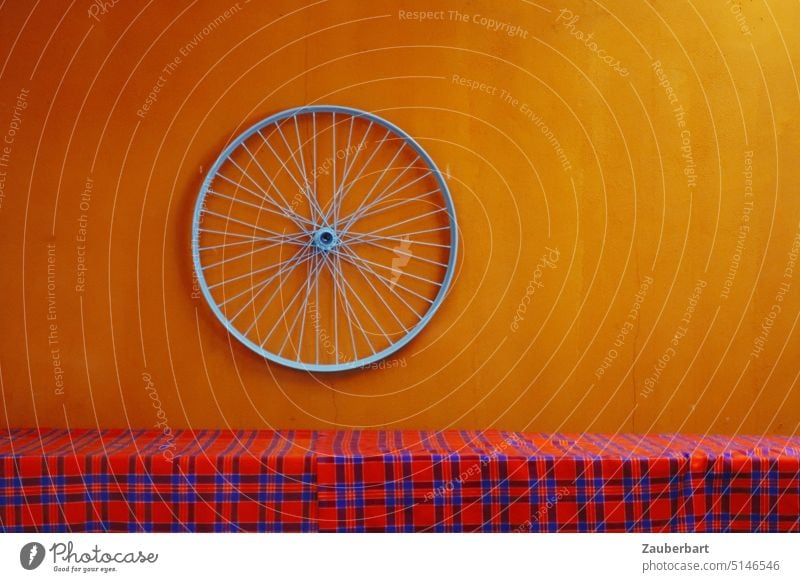 Rim of bicycle on orange wall in front of red checkered table cloth Wheel rim Bicycle Orange Red Checkered Massai Wall (building) Art Spokes Round Rotate