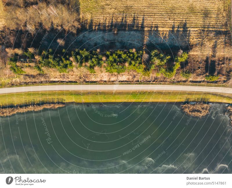 Sunset over a frozen lake. Sunbeams falling on water. Shadows of trees on the ice covering the lake. Aerial view of a frozen lake. Ice sheet background. Frozen grass in water