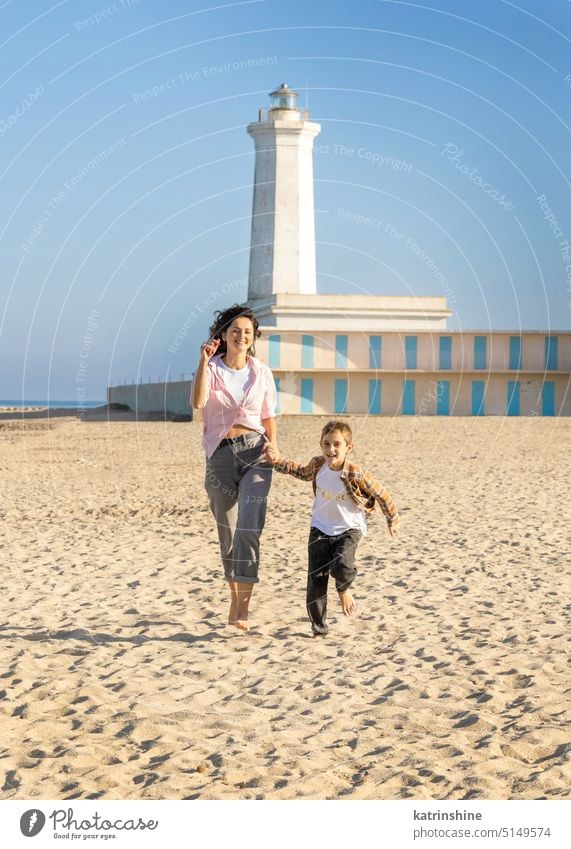 Happy Mother and son running on beach barefoot in a sunny day against the lighthouse sea sunset outdoor Toddler kid boy family together Mom fun smile sand