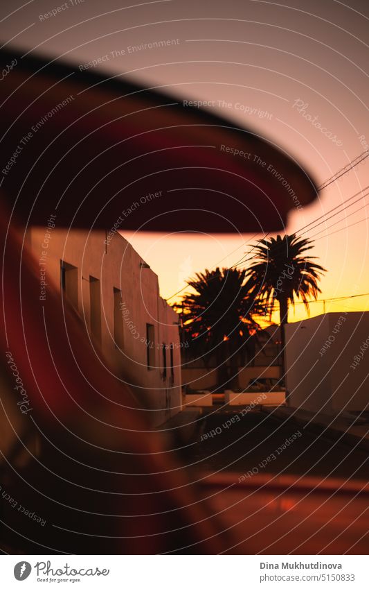 stack of surfboards on a car at sunset. Silhouette of surfboards on retro car roof and palm trees. Summer and surf background vertical wallpaper. Island life. Surfing relaxed lifestyle. Street in small surf village.