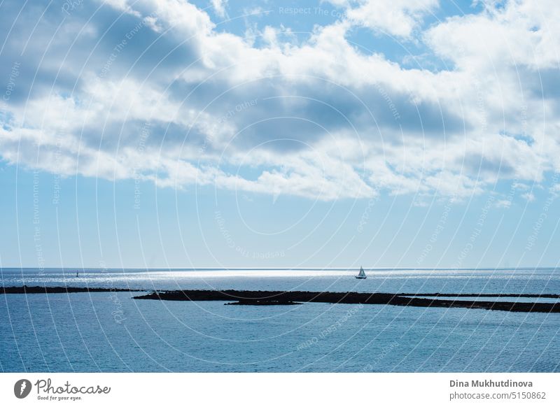 Seascape and cloudscape in blue color palette. Calm sea on a sunny day with clouds horizontal landscape background.  Distant boat silhouette in the ocean.