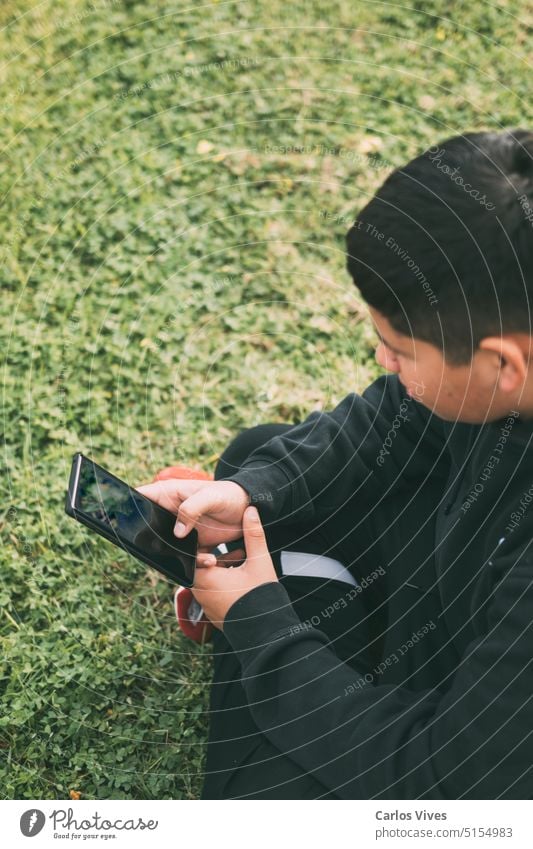 top view young boy sitting in the park, looking at his smart phone, selective focus adolescence call confidence connection connectivity contemplation