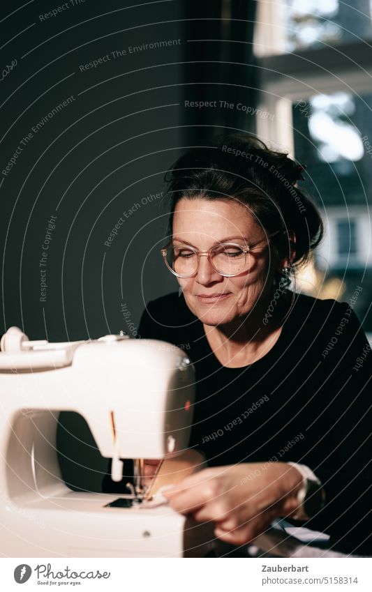 The seamstress IV - woman sitting at the sewing machine smiling and holding the fabric under the presser foot Woman concentrated Sewing machine Smiling hobby