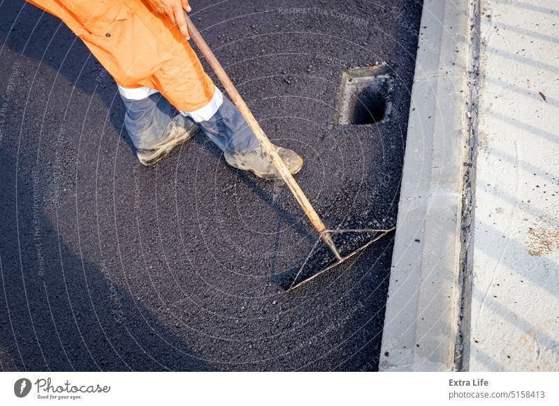 Worker rakes around the rainwater hole, levels the hot asphalt Above Align Alignment Asphalt Asphalting Bitumen Blacktop Blacktopping Bridge Building Site