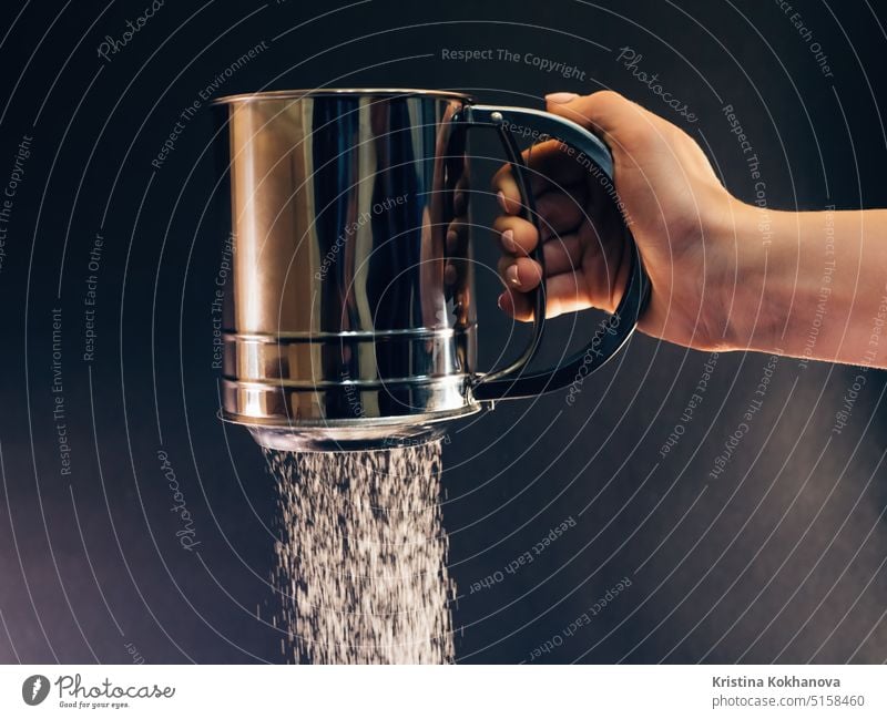 Female Hand sifting flour or sugar powder through sieve for baking. Close up baker bakery black blurred bowl bread burst cake caucasian chef closeup cloud color