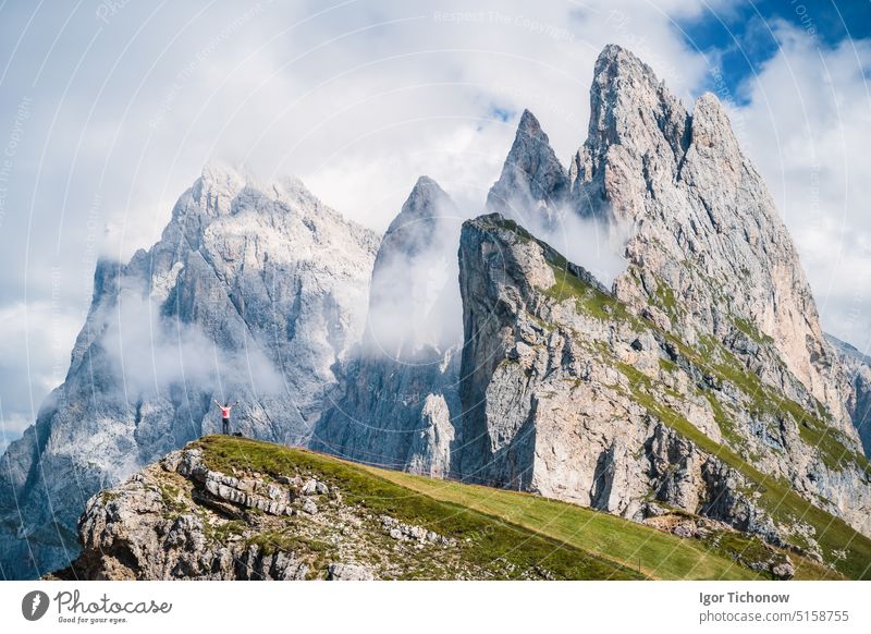 A man raising his hands in front of epic Furchetta and Sass Rigais peaks in Seceda, Dolomites Alps, Odle mountain range, South Tyrol, Italy, Europe. Travel vacation concept