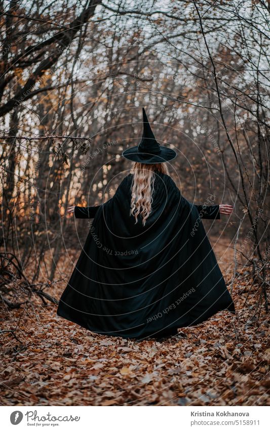 Blonde witch in long black cape and hat on autumn forest background. halloween girl horror spooky person woman dark child costume magic party fun death devil