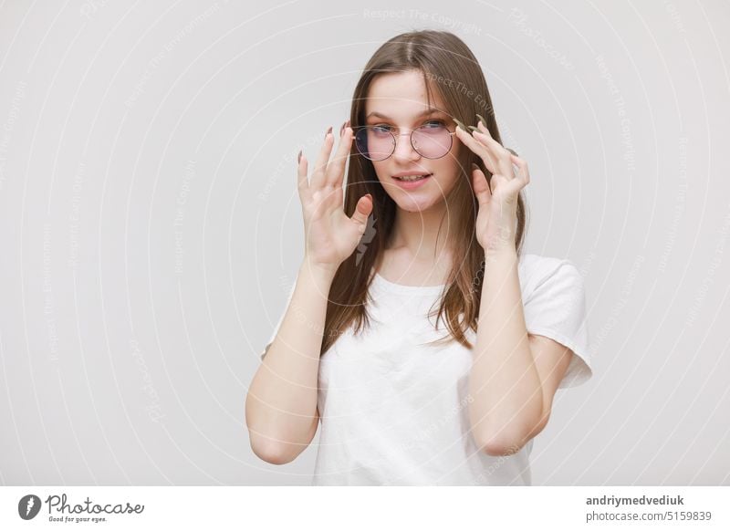 Focused frowning office girl staring at camera through eyeglasses on white background. Young woman adjusting eyewear. Glasses wearing concept business fashion