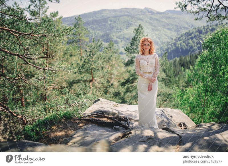 beautiful young red-haired bride in the forest with a floral wreath on her head. woman in long white dress outdoors on summer day. wedding day woods bouquet