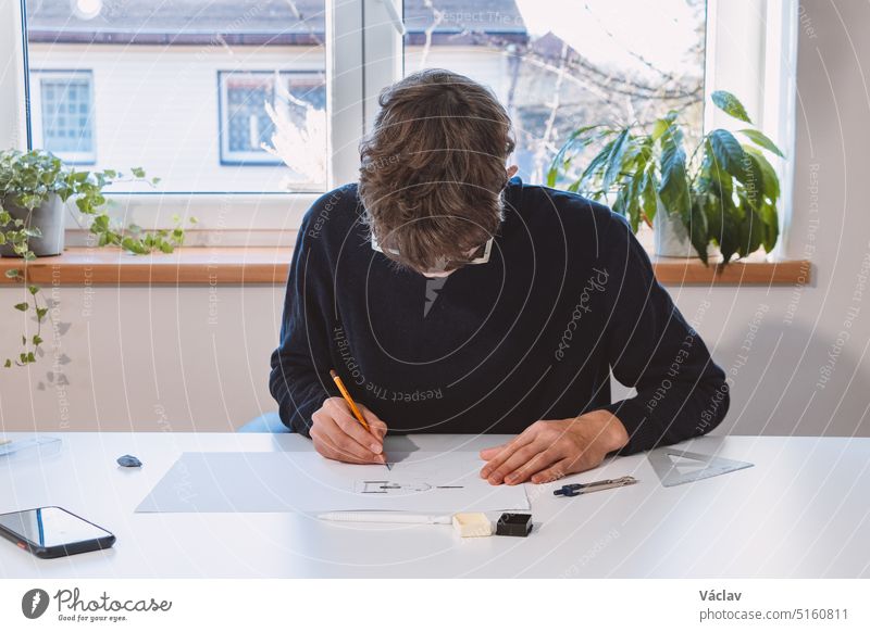 Brown-haired young architect creates new product designs for a new futuristic world. Working with your own creativity. Compass, pencil, ruler and paper. Creative home office