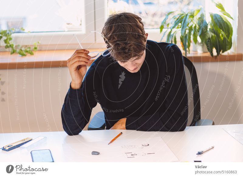 Brown-haired architect is thinking hard about a new design for a new prototype, which he draws in pencil on paper. Inventing a new design. An ambitious young boy. Illuminated workroom