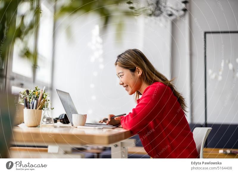 Young woman sitting at desk working on laptop real people millennials student indoors loft window natural girl adult one attractive successful confident person