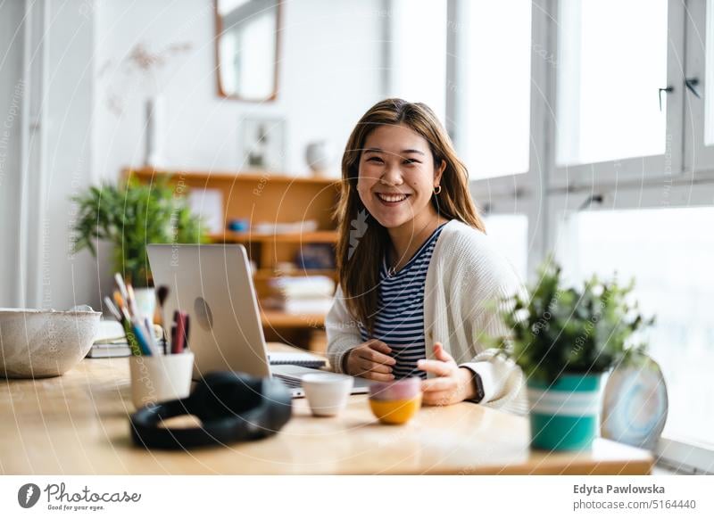 Young woman sitting at desk working on laptop real people millennials student indoors loft window natural girl adult one attractive successful confident person