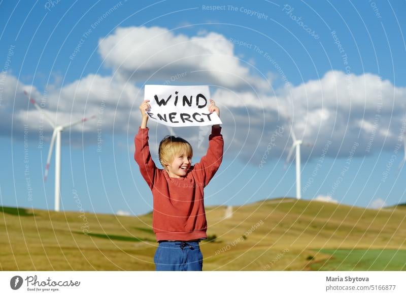 Eco activist boy with banner "Wind Energy" on background of power stations for renewable electric energy production. Child and windmills. Wind turbines for generation electricity. Green energy