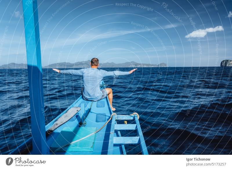 Back view of the man on boat with spreading hands arriving to exotic tropical island lit by sun light. Travelling tour in Asia: El Nido, Palawan, Philippines