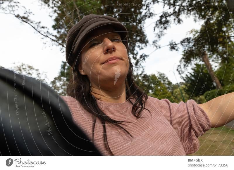 Brunette woman with brown cap looks down to camera smiling from under cap shield women smiled smiling woman Feminine Adults pretty Long-haired Face portrait